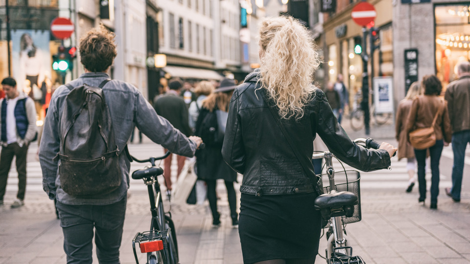 Couple walking with city bikes in Copenhagen street shopping. Urban living lifestyle. Commuting with bicycle, young students couple tourists traveling in Europe.