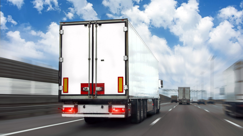 Truck with a white trailer drives motion blur effect speed along the highway in heavy traffic in the with clouds in the sky