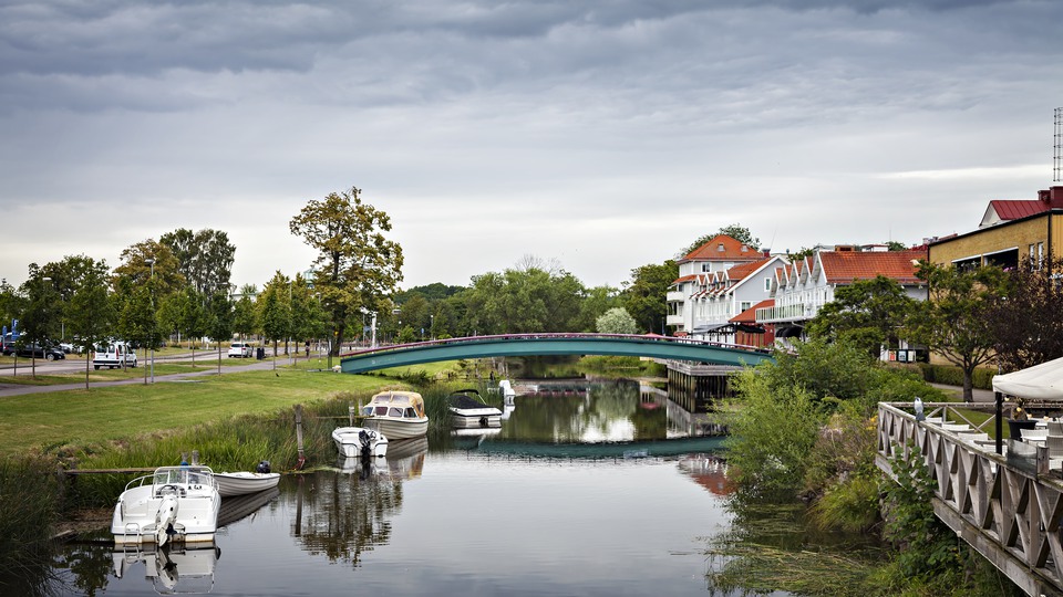 Älvstranden i Kungsbacka, utanför Göteborg. En bro korsar en liten flod med några båtar förtöjda vid sidan om.  Hus till höger om bron och en väg till vänster.