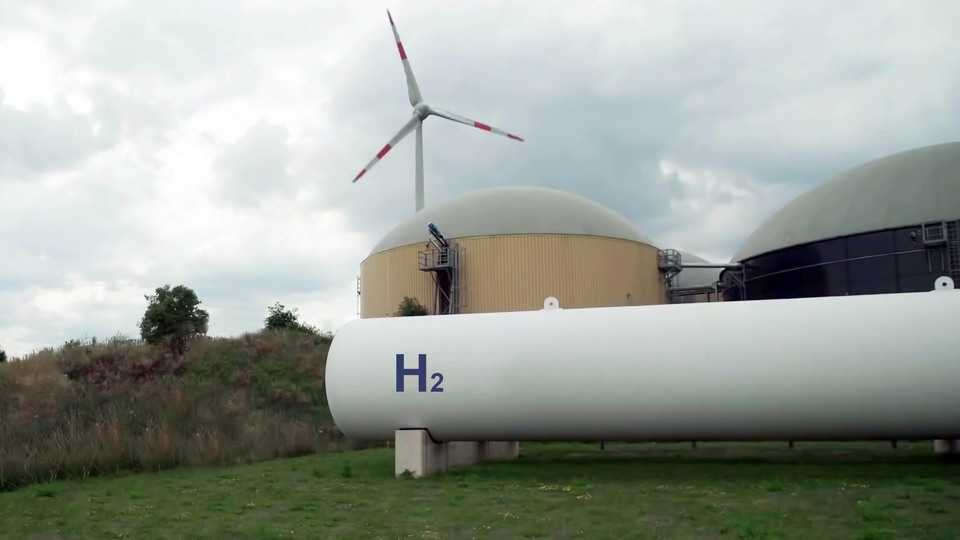 view of a hydrogen storage, with a hydrogen tank. And in the background a wind turbine.